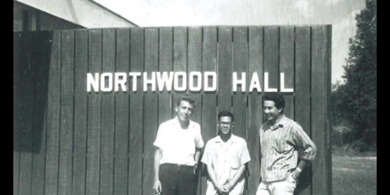 Three men stand under a sign that reads "Northwood Hall"