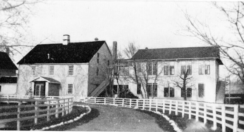 A curved road lined with a fence leads to two buildings.