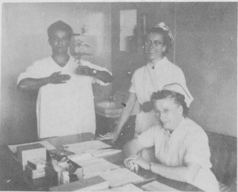 A woman sits at a desk and a man and woman stand next to her.