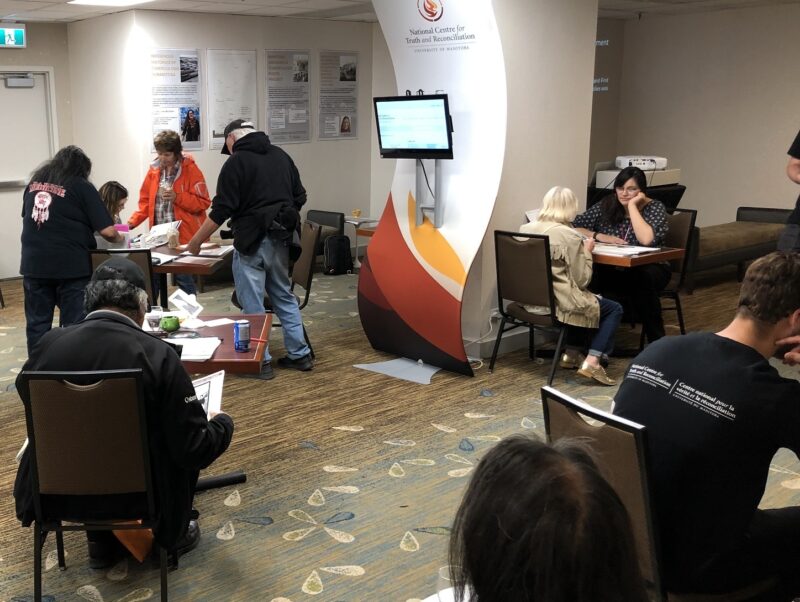 A group of people look at books at four tables scattered around a room