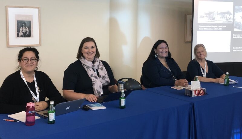 Four women sitting in a row at a table with a blue tablecloth