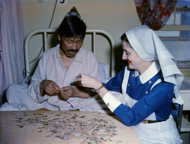 An Indigenous man in a hospital bed does a puzzle with the assistance of a white nurse