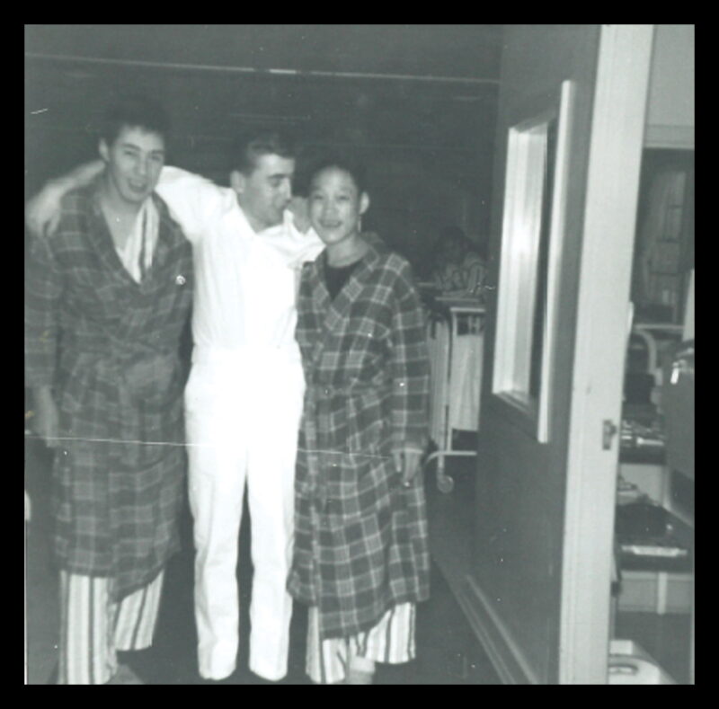 A man puts his arms around two young men in plaid robes.