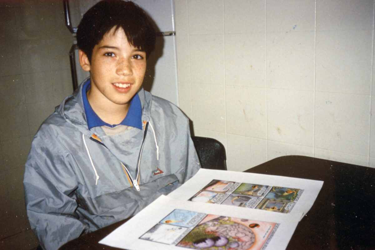 A boy with illustrated pages on the table in front of him.