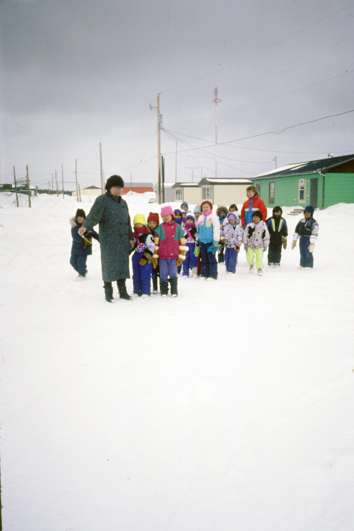 A group of school children children with two women outdoors in the snow.