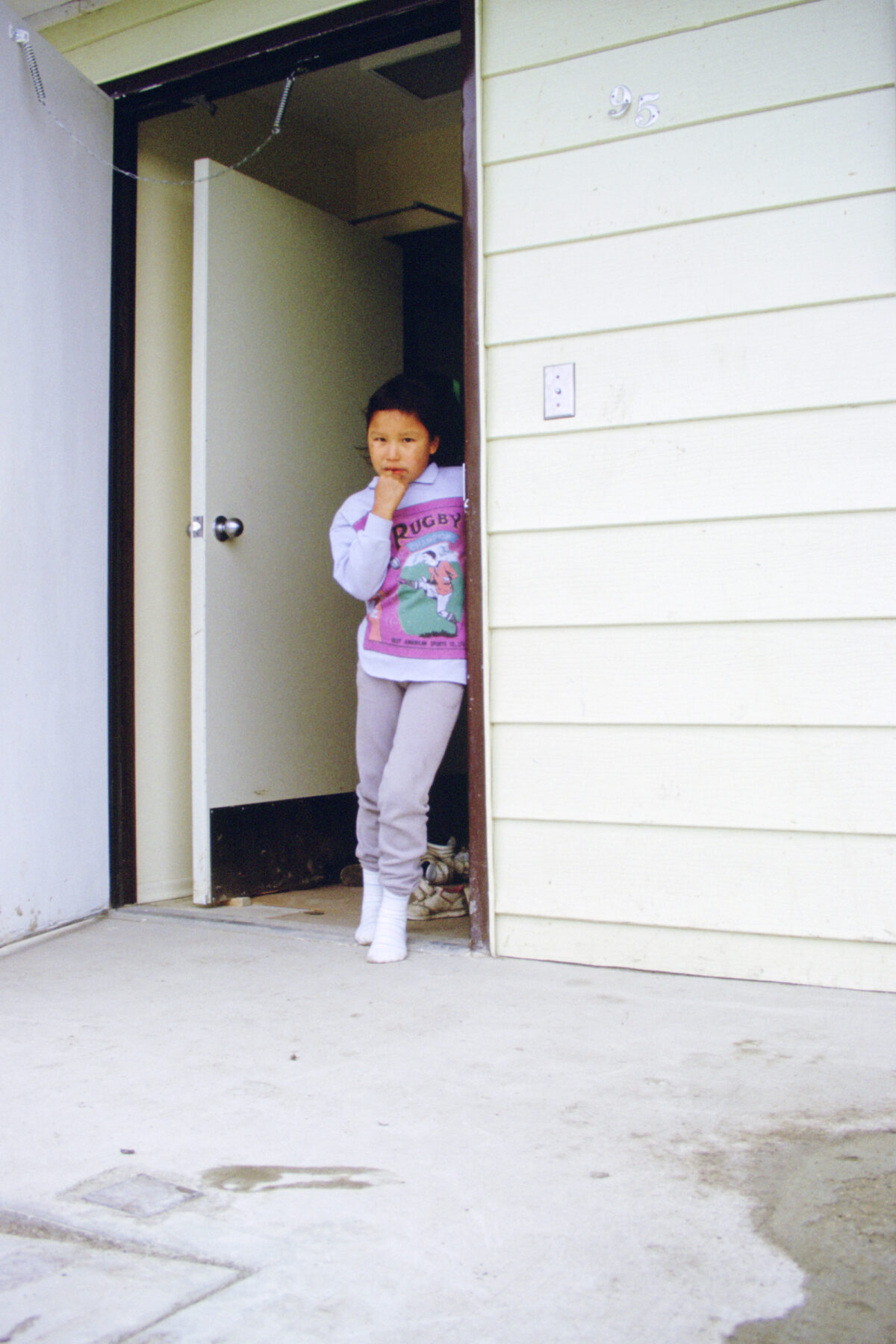 A child in a "rugby" sweatshirt standing in a doorway.