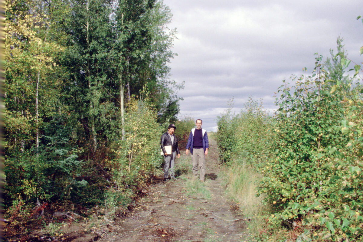 Two people on a dirt path in a wooded area.