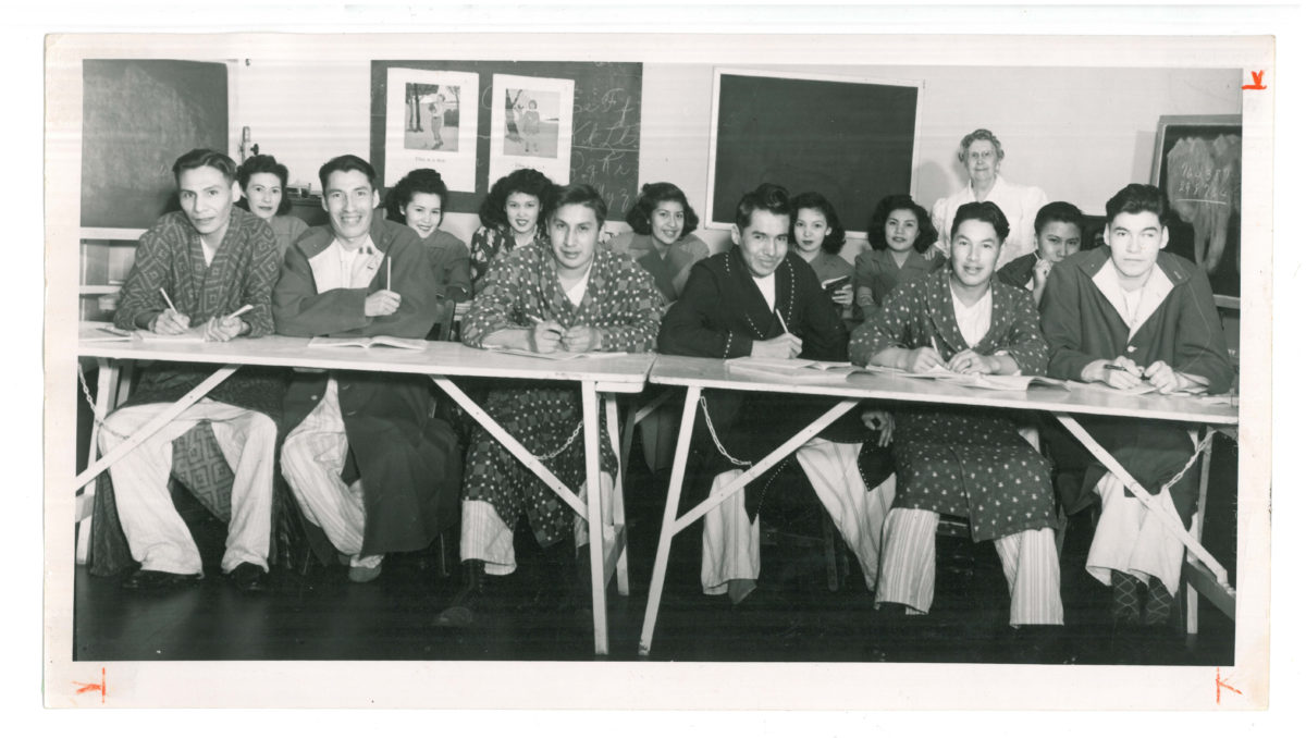 Group of patients sitting at tables in a classroom with nurse teacher in background