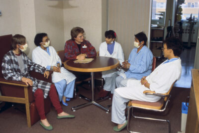 Six people sitting around a table. Three people are wearing facemasks.