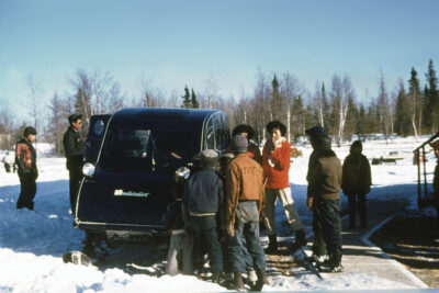 A group of people next to a Bombardier snow mobile