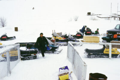 A man walks amongst a group of parked snowmobiles.