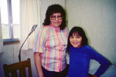 A woman in a multi-coloured striped shirt stands next to a girl in a blue sweater.