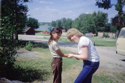 A woman holds a young woman's arm outdoors. They both look at the camera.