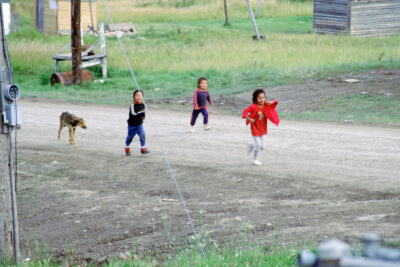 Three children and a dog running down a road.