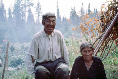 A man and woman sit outside in a forested area.