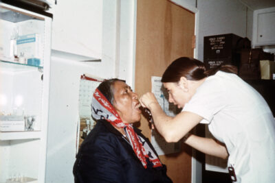 A nurse inserts a tongue depressor in a woman's mouth.