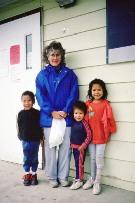 A woman in a blue coat stands next to three children at the entrance of a building.