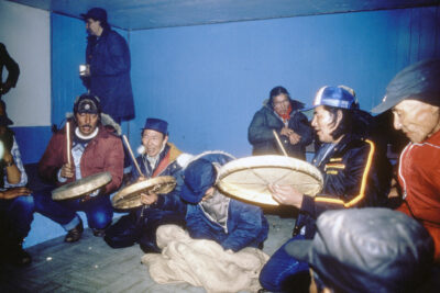 A group of men in a drumming circle. Three men are holding drums and singing.