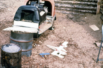 The back of an open vehicle on treads. Two barrels sit behind the vehicle, and a toy airplane sits on the ground next to them.