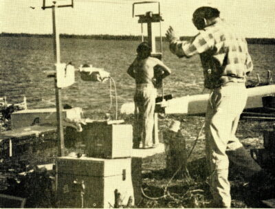 A child presses his chest against an x-ray plate outdoors next to a lake. A man in a plaid shirt stands next to the child and operates the machine.