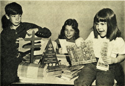 Three children hold Christmas Seal stamps, next to stacks of more stamps.