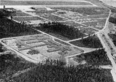 An aerial view of a collection of long buildings, surrounded by trees.