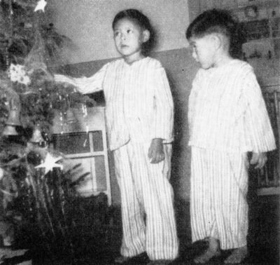 Two boys in striped pyjamas stand next to a christmas tree