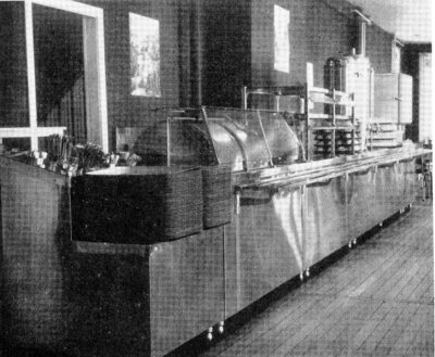 A cafeteria counter with a stack of trays in the foreground.