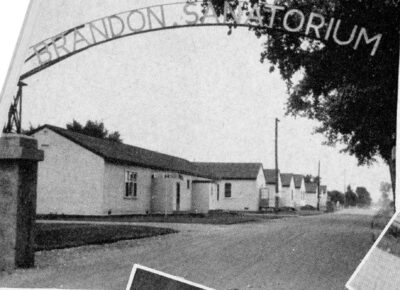 A row of single-storey buildings stand along a road. A curved sign arches over the road and reads, "Brandon Sanatorium."