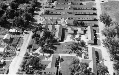 An aerial view of long, single-storey buildings with trees throughout.