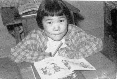 A child sits at a desk with a picture book in front of her. She rests her arms on the desk.