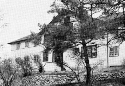 A view of a building, with a tree in the foreground. The landscape in front of the building is lined with stones.