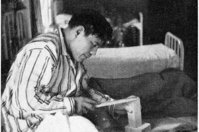 A man in striped pyjamas sits on a hospital bed and carves a piece of soapstone.