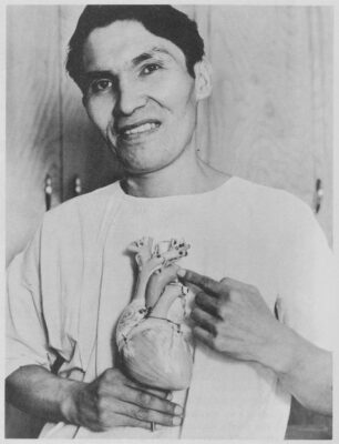 A man holds a model heart up to his chest.
