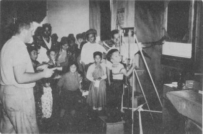 A young boy presses his chest on an x-ray plate while a group of people watch.