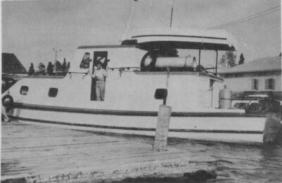 A docked boat. A person can be seen standing at the boat's doorway.