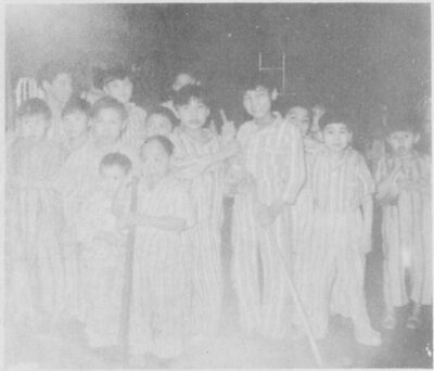A group of young boys in striped pyjamas. Two boys hold a mop.