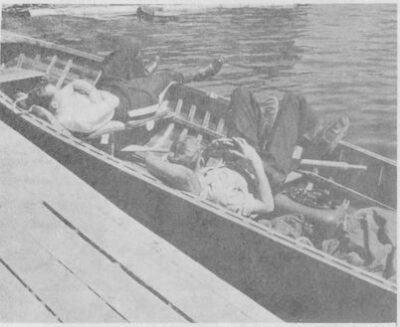 Two men sleep in a docked canoe.