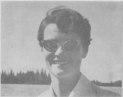 A portrait of a woman wearing cat-eye sunglasses at a lake.
