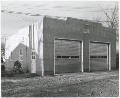 The exterior of a building with two garage doors and a flat roof. Powerlines cross above the building,
