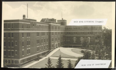The exterior view of a building with trees in the foreground. Labels on the photo read: "Back Wing Extending (Chapel) // Rear View of Sanatorium"