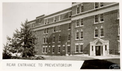 The exterior view of a building with a small tree in the foreground. A label on the photo reads: "Rear entrance to the Preventorium"