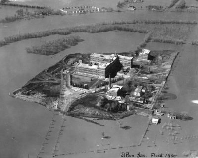 An aerial view of a flooded landscape. At the centre is a complex of buildings. An annotation reads: "St Bon. San. Flood 1950"