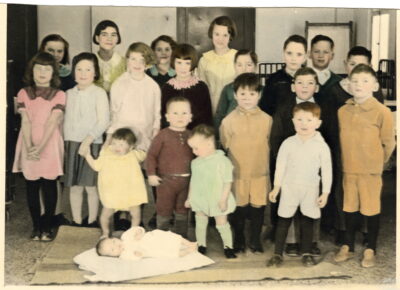 A colourized photo of a group of children. Hospital beds can be seen in the background.