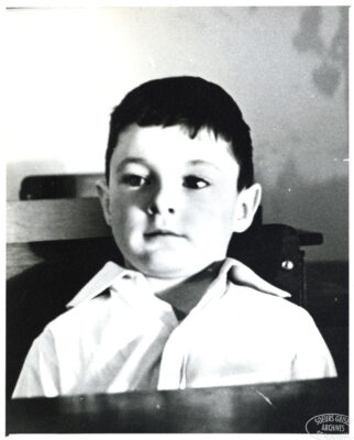 A portrait of a boy sitting at a desk, leaning back in his chair.