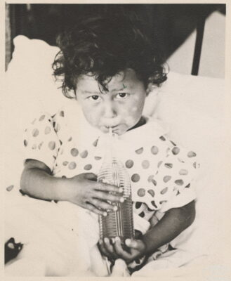 A child with a polka-dot shirt drinks from a bottle.