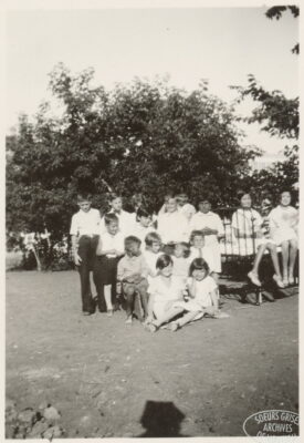 A group of children ouside on the grass. Some children sit on a hospital bed.