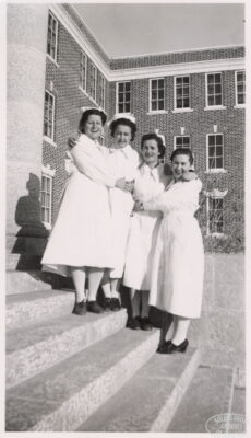 Four nurses hug each other on the steps of a builiding.