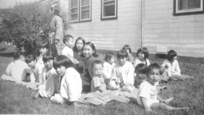 A group of children sit on the grass next to a building.
