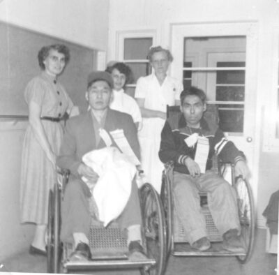 Two men sit in wheelchairs. Three women stand behind them.